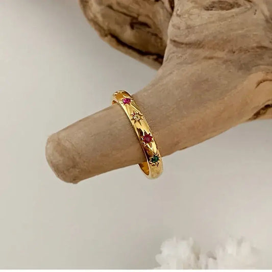Gold bracelet with red and green stones on a wooden surface