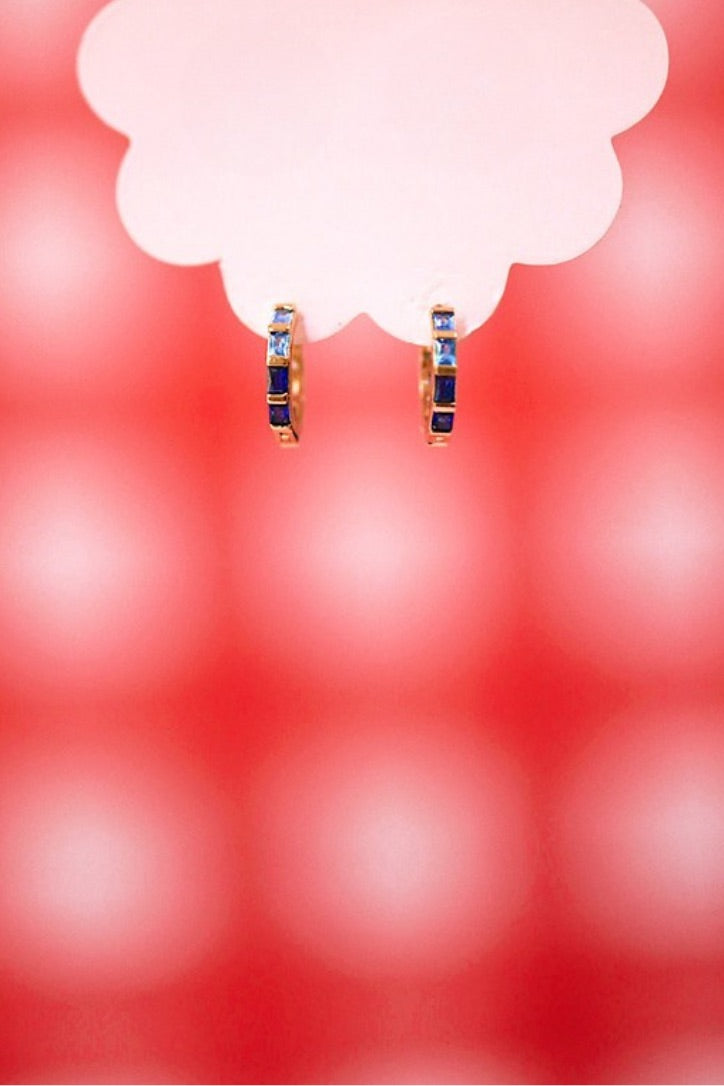 Gold hoop earrings with blue stones on a red and white background