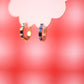 Gold hoop earrings with blue gemstones on a blurred red background