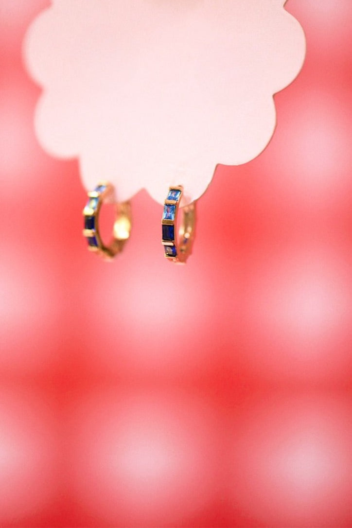 Gold hoop earrings with blue gemstones on a blurred red background