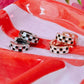 Pair of checkered earrings on a red and white striped surface with flowers in the background
