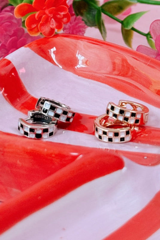 Pair of checkered earrings on a red and white striped surface with flowers in the background
