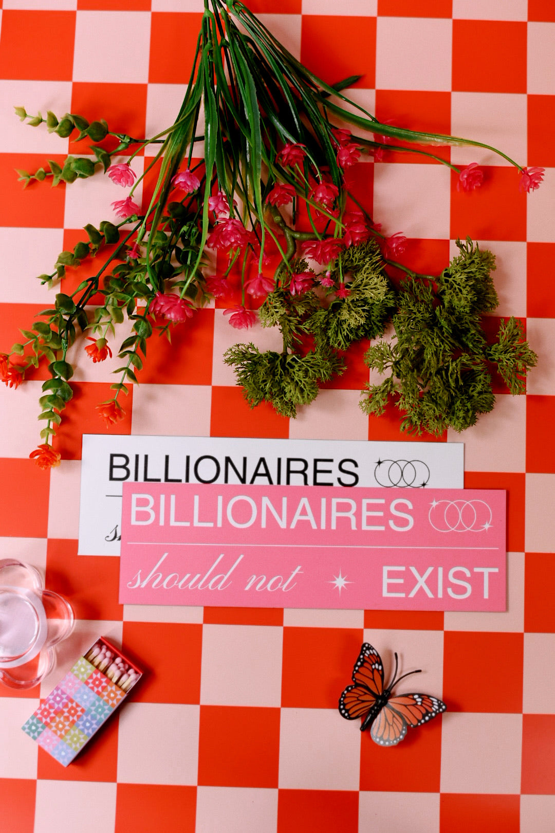 Floral arrangement on a red and white checkered tablecloth with 'Billionaires Should Not Exist' sign.