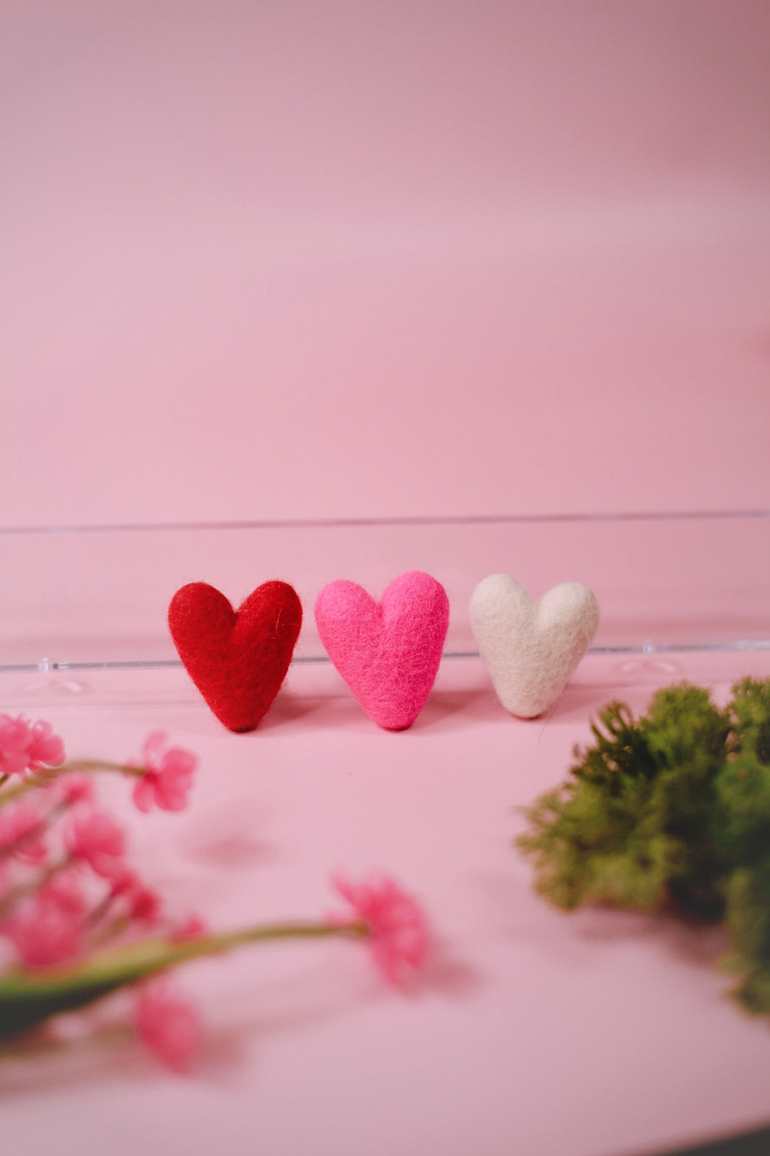 Three heart-shaped objects on a pink surface with blurred flowers and greenery in the foreground.
