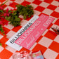 Two pink signs with text on a red and white checkered tablecloth.