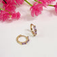 Gold hoop earrings with purple stones on a white background with pink flowers.