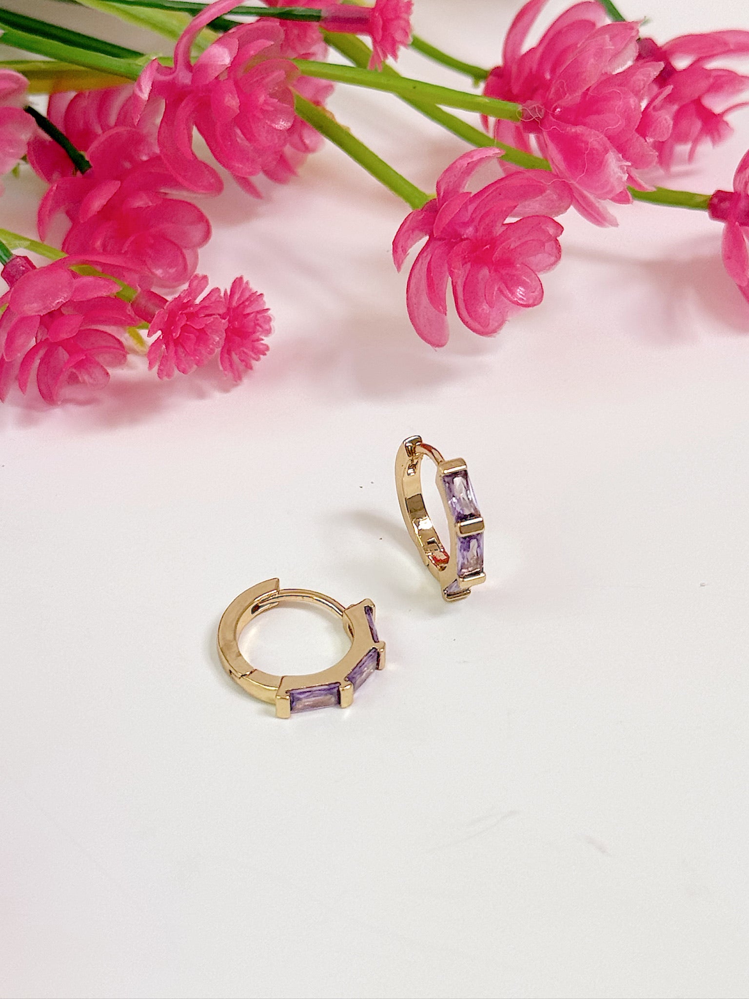 Gold hoop earrings with purple stones on a white background with pink flowers.