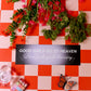 Floral arrangement on a red and white checkered tablecloth with a humorous sign.