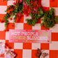 Floral arrangement on a red and white checkered tablecloth with a humorous sign and butterfly.