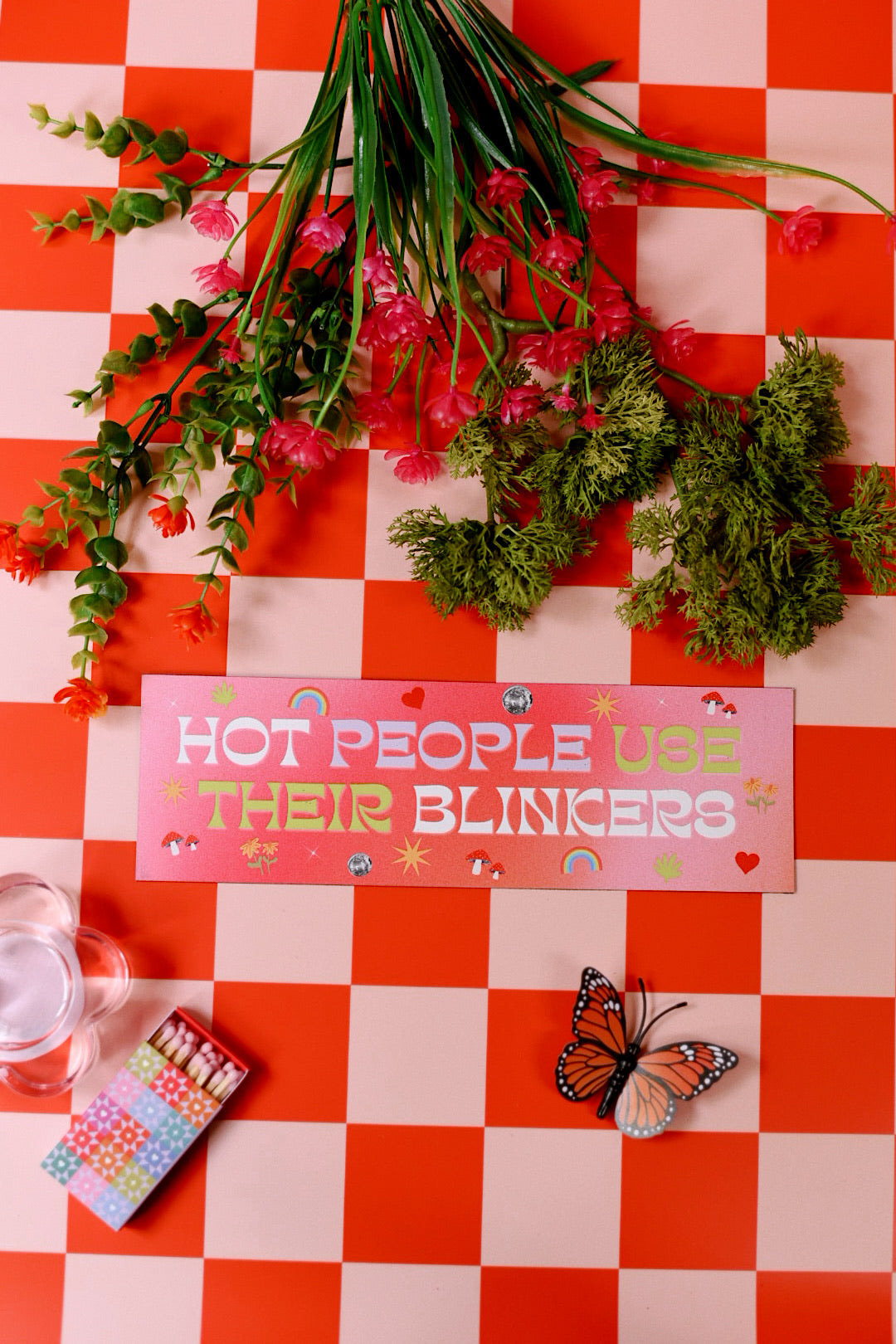 Floral arrangement on a red and white checkered tablecloth with a humorous sign and butterfly.