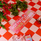 Car bumper magnet on a red and white checkered tablecloth with flowers and a butterfly.