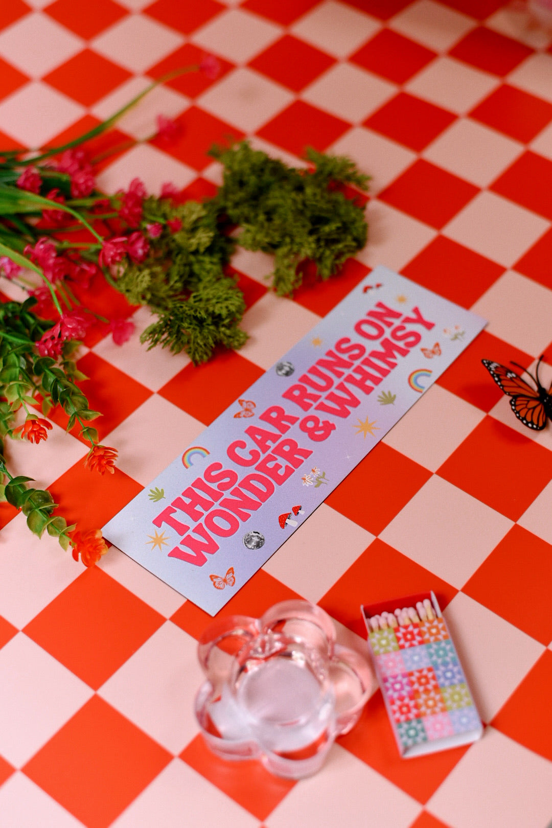 Decorative sign with text on a red and white checkered tablecloth with flowers and a butterfly.