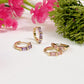 Gold hoop earrings with gemstones on a white surface with pink flowers and greenery.