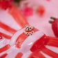 Two gold rings with checkered patterns on a red and white striped surface with blurred flowers in the background.