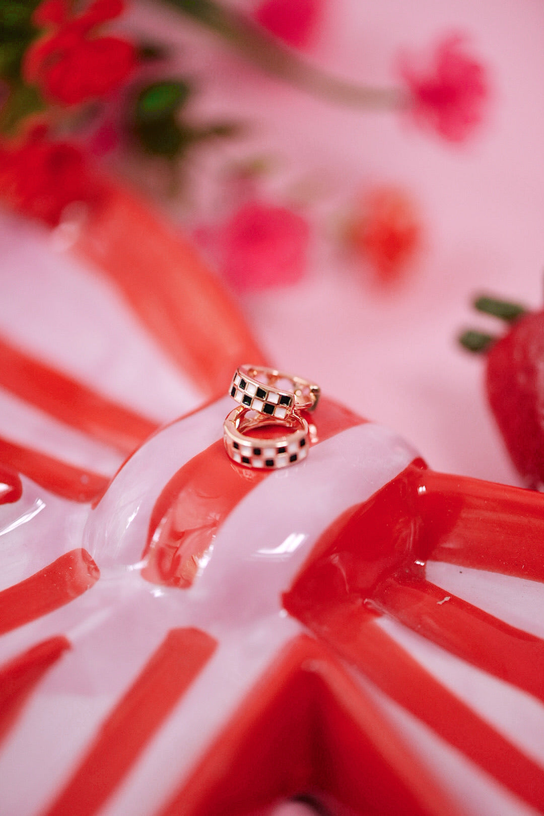 Two gold rings with checkered patterns on a red and white striped surface with blurred flowers in the background.