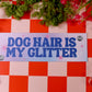 Sign with 'Dog Hair is My Glitter' on a red and white checkered tablecloth with flowers and a matchbox.