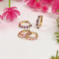Gold hoop earrings with pink and purple gemstones on a white surface with pink flowers in the background.