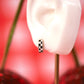 Close-up of a white ceramic ear with a small checkered earring on a red floral background