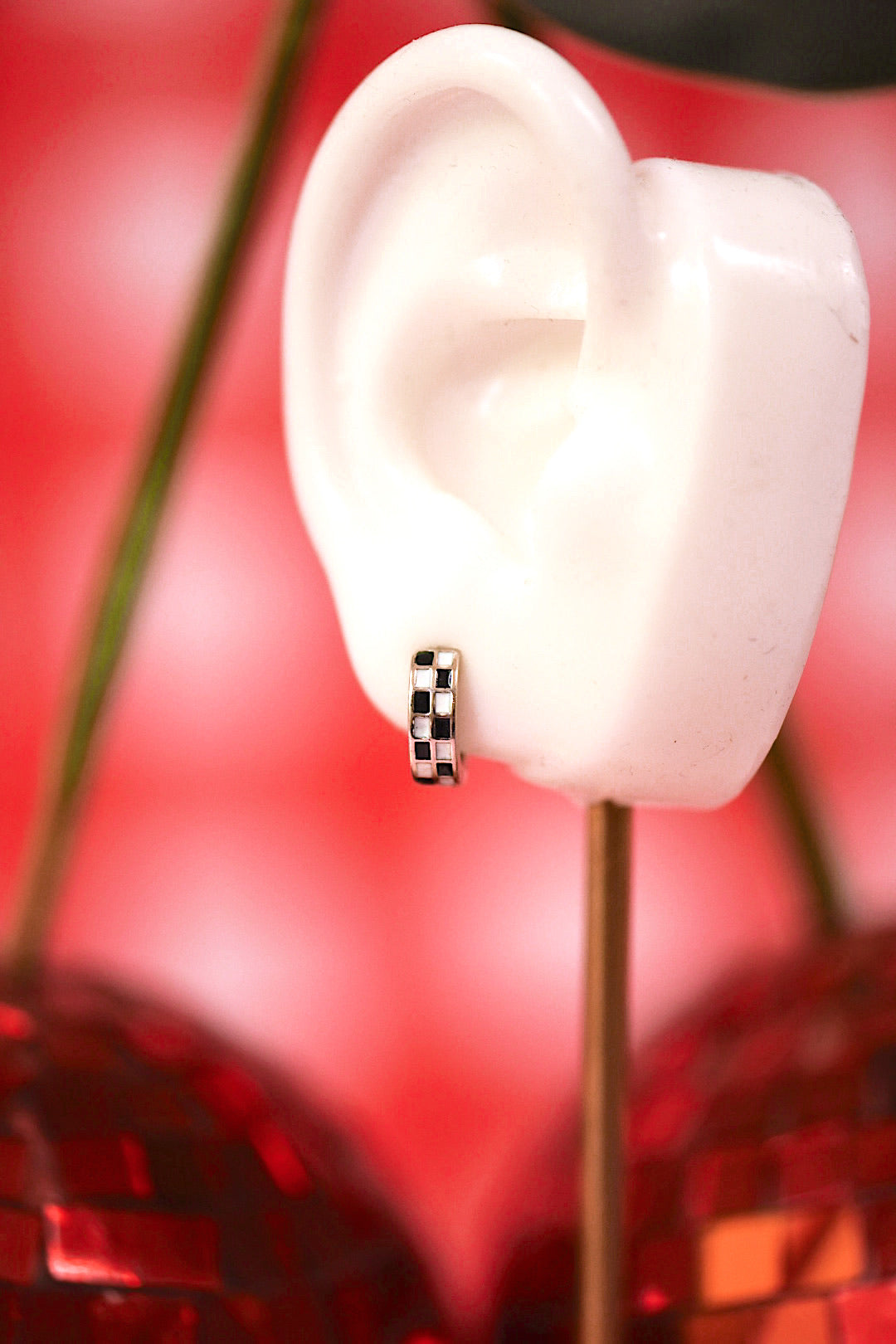 Close-up of a white ceramic ear with a small checkered earring on a red floral background